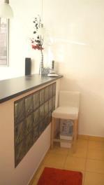 Světlý barový kout se skládá ze skleněné zdi a dlažby, doplněný moderním nábytkem a dekorativními prvky, nabízí útulný a stylový design.