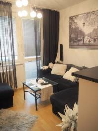 Světlý obývací pokoj s parketovou podlahou, velká okna a moderní sedačka. Skandinávský styl s elegantními závěsy a dekoracemi.