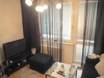 Obývací pokoj s parketovou podlahou, velkými okny a moderním nábytkem, nabízí útulné prostředí s minimalistickým designem.