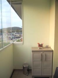 Zasklený balkón s dlažbou, výhledem na město a horami v pozadí, vybavený úložnou skříňkou a dekorativní květinovou výzdobou.