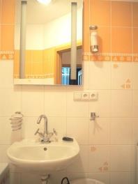 Kompaktní koupelna s bílým keramickým umyvadlem, světle oranžovým obkladem a moderním osvětlením nad zrcadlem.