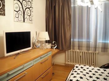 Malá ložnice s parketovou podlahou, moderní výzdobou a velkým oknem s žaluziemi.