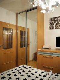 Prostorná ložnice s velkými zrcadlovými dveřmi, parketovou podlahou a moderní vestavěnou skříní, elegantní osvětlení zajišťuje světlý interiér.