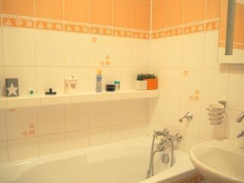 Koupelna s bílými dlaždičkami a oranžovým dekorem, vana a umyvadlo, světlá a udržovaná, moderní styl.